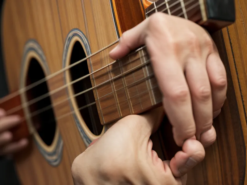 Primer plano de manos intentando poner un acorde difícil en una guitarra acústica.